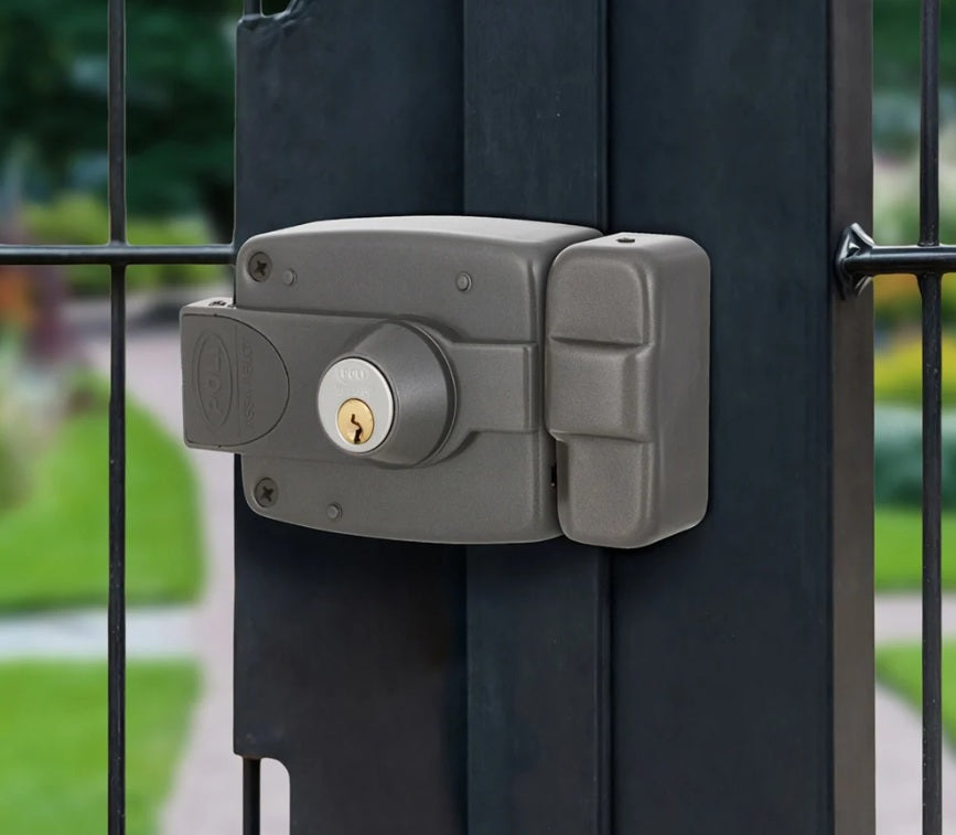 Cerradura eléctrica sobreponer Poli 3010 instalada con caja para soldar en reja metálica exterior de portón o acceso.